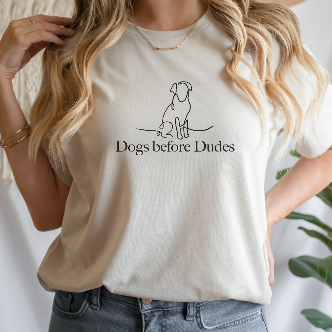 "Dogs before dudes text and graphic design centered on natural t-shirt."