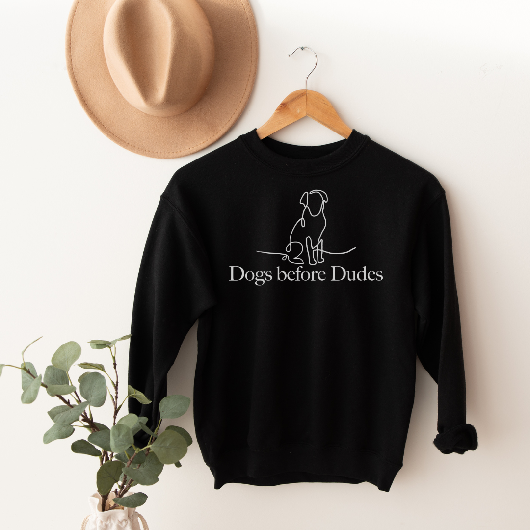 "Dogs before dudes text and graphic design centered on black sweater."